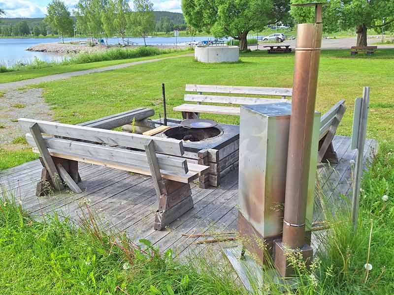 Eine gemauerte Feuerstelle mit Holzbänken am Ufer.